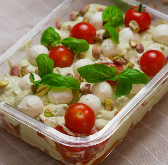 Tomaten-Mozzarella-Tiramisu in einer gläsernen Auflaufform auf einem Tisch, daneben frisches Basilikum