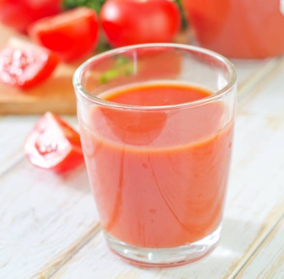 Ein Glas Tomatensaft selbst gemachter Tomatensaft vor einer Karaffe auf einem Holztisch, daneben frische Tomaten