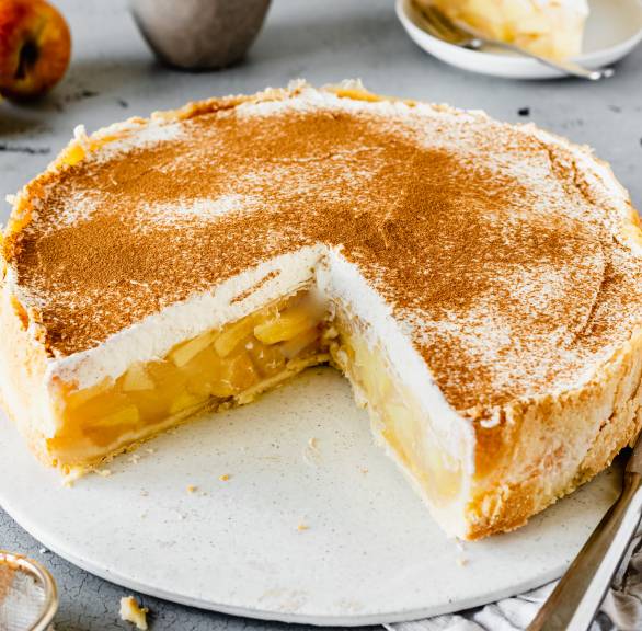 Runde Apfel-Wein-Torte mit Vanillesahne angeschnitten auf einer Tortenplatte bestäubt mit Zimt