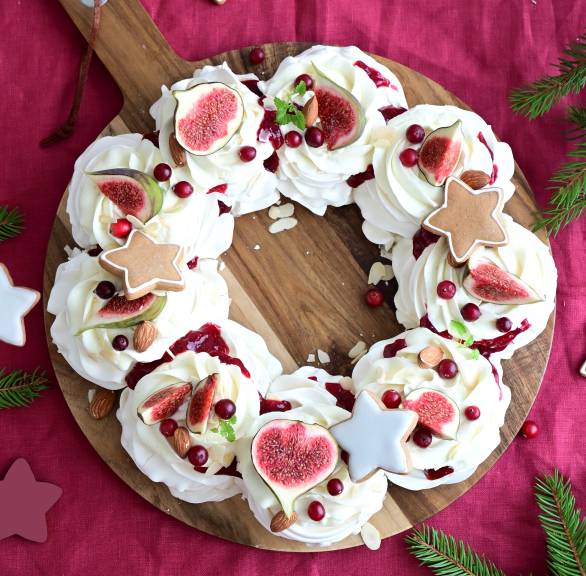 Weihnachts-Baiserkranz mit Mascarponecreme getoppt von Cranberry-Kompott, dekoriert mit frischen Feigen, Mandeln und Lebkuchensternen auf einem Holzbrett