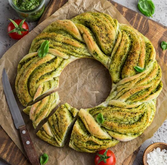 Selbst gebackener Brotkranz mit grünem Basilikum-Pesto angeschnitten auf einem Holzbrett