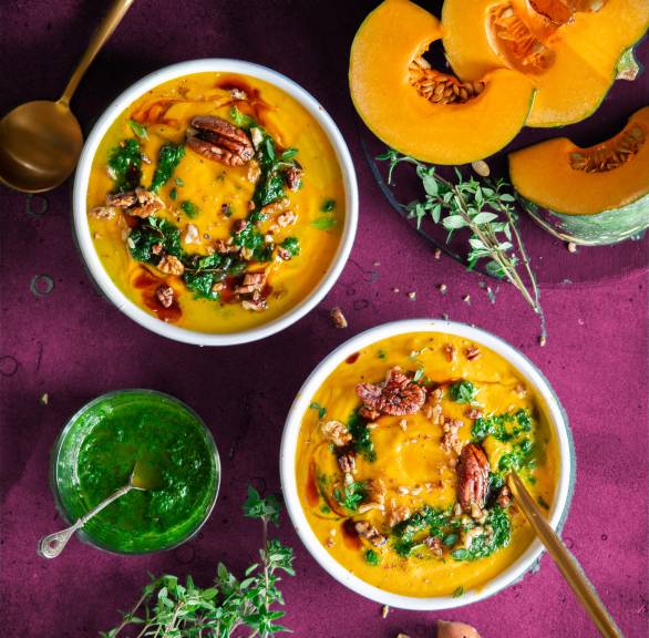 Selbstgekochte Kürbis-Ingwer-Suppe angerichtet in zwei Suppentellern getoppt von Kräuteröl und Nüssen