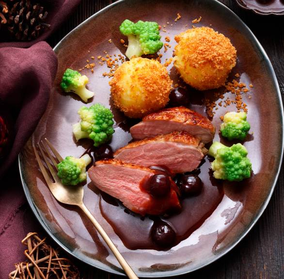 Entenbrustfiletstücke festlich angerichtet auf einem Teller mit Romanesco und panierten Klößen übergossen mit Amarenasoße