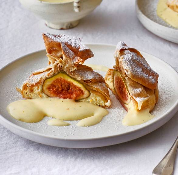 Halbiertes Filoteig-Päckchen gefüllt mit ganzen Feigen und Ricotta auf einem Bett aus Limetten-Zabaione auf einem Dessertteller