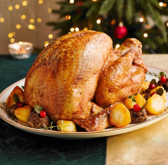 Ganze gefüllte Poularde auf einer Servierplatte umgeben von Hackbällchen, Kartoffeln und Früchten