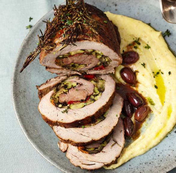 Rollbraten mit mediterraner Gemüsefüllung angeschnitten auf einer Servierplatte, daneben Polenta