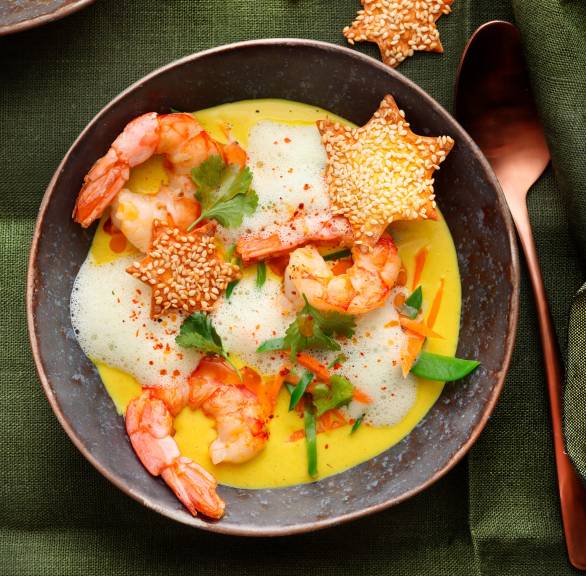 Karottencremesuppe in mehreren Suppentellern getoppt von gebratenen Garnelen, Wan Tan-Knuspersternen und Milchschaum auf einem weihnachtlich dekorierten Tisch