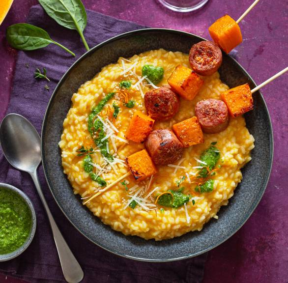 Butternutkürbis-Risotto getoppt mit Salsiccia-Spießen auf einem Tisch