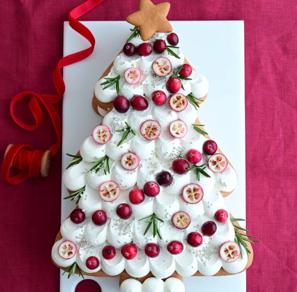 Weihnachtsbaum aus Honigkuchen mit weißem Frosting und Deko auf einer Tortenplatte