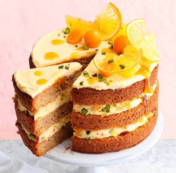 Italienische Lebkuchen-Weihnachtstorte mit Orangencreme und Pistazien angeschnitten auf einer Tortenplatte dekoriert mit Physalis und Orangenscheiben