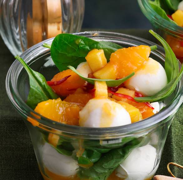 Mehrere Gläser mit Mozzarella auf Blattspinat und Orangen-Chutney auf einem Tisch, daneben Grissini