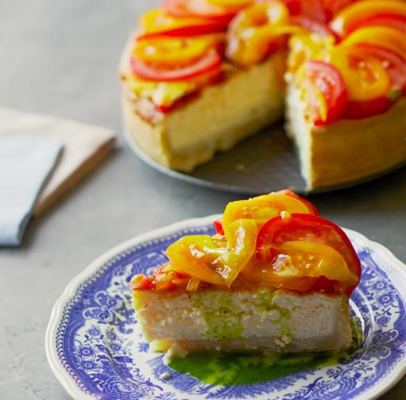 Ein Stück Parmesan-Tarte getoppt mit Tomatensalat auf einem Teller, dahinter die restliche Tarte angeschnitten