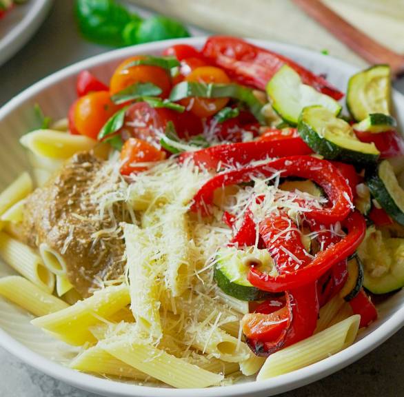 Pasta-Bowl mit Ofengemüse auf einem tiefen Teller, daneben geriebener Parmesan