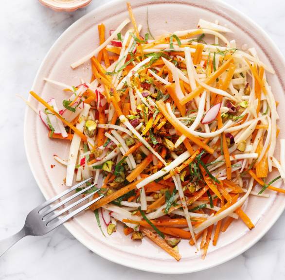 Roher Karottensalat mit Pastinaken, Radieschen und Pistazien auf einem Teller, daneben Orangendressing