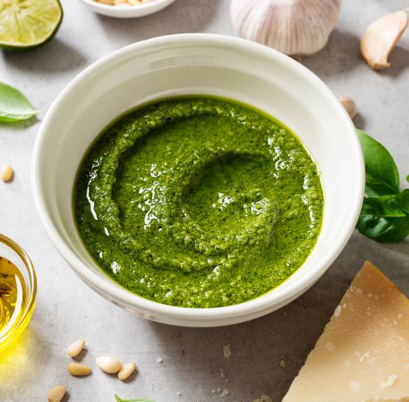 Selbstgemachtes Basilikumpesto alle Genovese in einer Schale, drumherum einige Zutaten wie Olivenöl, Pinienkerne und Käse