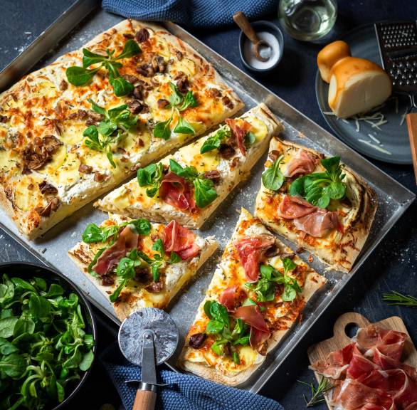 Weiße Pizza Bianca belegt mit Kartoffeln, Maronen, Feldsalat und Parmaschinken angeschnitten auf einem Backblech