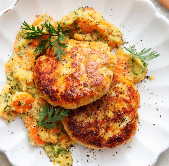 Zwei gebratene Putenfrikadellen mit Quark und Haferflocken auf einem Teller mit Karottenpolenta