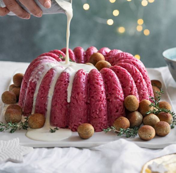Rosa Risotto-Gugelhupf auf einer Servierplatte umgeben von Polpette wird gerade mit Gorgonzolasauce übergossen