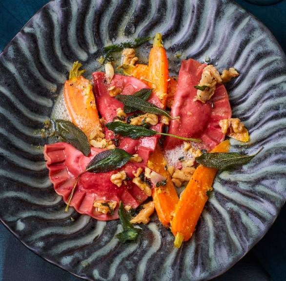 Selbst gemachte Rote Bete-Ravioli mit Käsefüllung angerichtet auf einem Teller mit Ingwer-Karotten und Walnusstopping