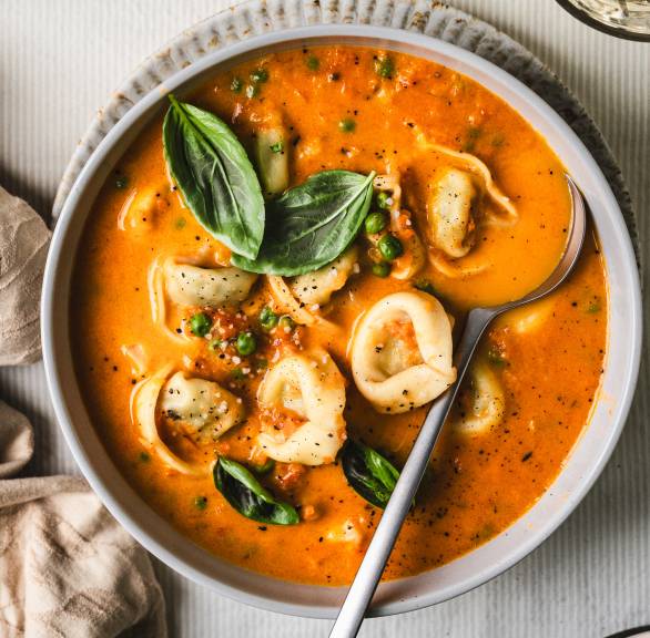 Selbstgekochte, cremige Tomatensuppe mit Erbsen und Tortellini in einer Suppenschüssel von oben