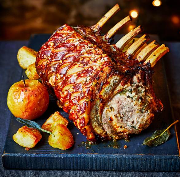 Schweinekotelette-Braten mit Semmelknödel-Füllung angerichtet auf einer Servierplatte, daneben Bratäpfel und Kartoffeln