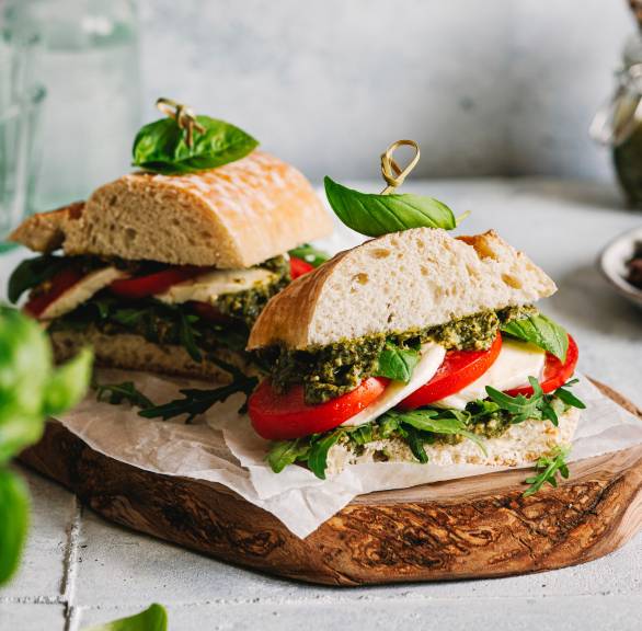 Zwei Panini-Brot belegt mit Tomate, Mozzarella und Basilikumpesto angerichtet auf einem Holzbrett