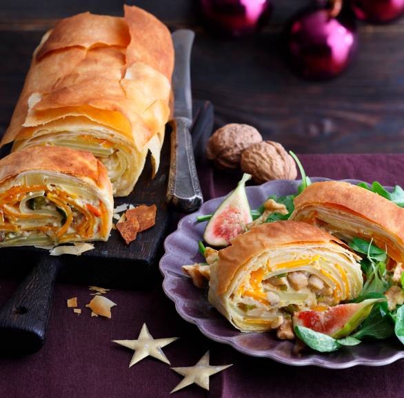 Veganer Kürbisstrudel gefüllt mit Pilzen und Kartoffeln angeschnitten auf einer Platte, davor ein Stück auf einem Teller