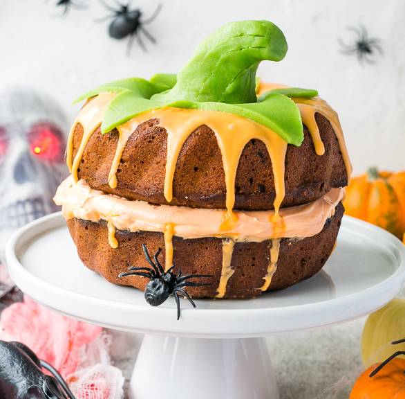Kuchen, der aussieht wie ein Kürbis auf einer Kuchenplatte auf einem für Halloween dekorierten Tisch