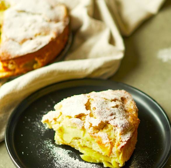 Ein Stück italienischer Apfelkuchen nach Torta die Mele Rezept auf einem Kuchenteller, dahinter der Rest des Kuchens