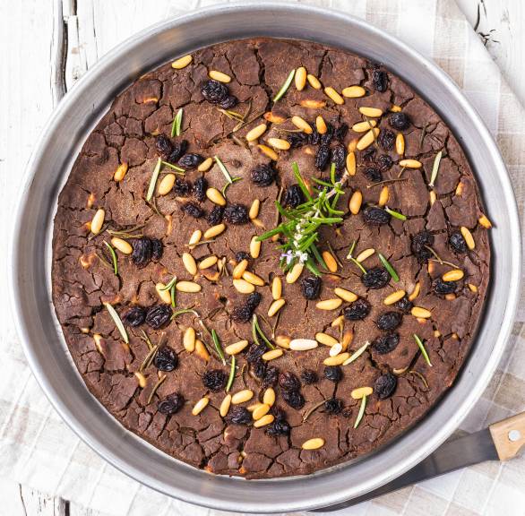 Italienischer Kastanienmehlkuchen Castagnaccio bestreut mit Rosinen und Pinienkernen in einer Springform
