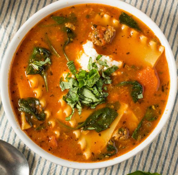 Eine Portion Lasagne-Suppe in einem Suppenteller getoppt von Crème fraîche und frischem Basilikum auf einem Tisch