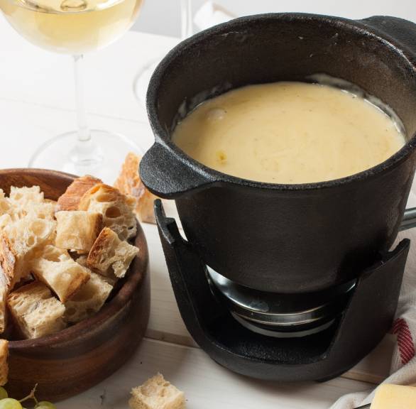 Fonduta, italienisches Käsefondue, in einem Fonduetopf, daneben Käse und Trauben auf einem Tisch