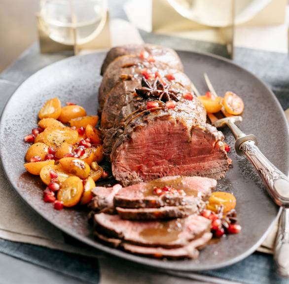 Rinderbraten angeschnitten auf einer Platte garniert mit karamelliserten Früchten, daneben Rotweinsoße