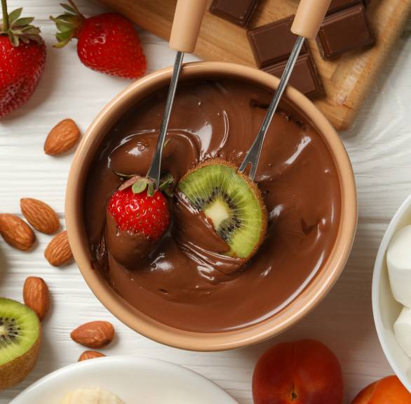 Schokofondue in einem Topf auf einem Tisch, drumherum Obst und Marshmallows zum Dippen