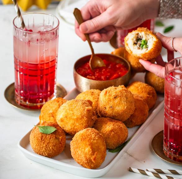 Arancini mit Hackfleisch-Erbsenfüllung auf einem Buffet, daneben Tomatensalsa