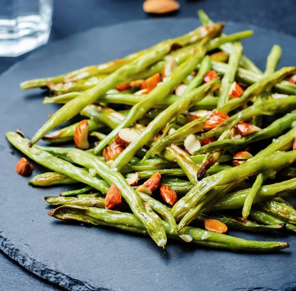 Gebratene grüne Bohnen bestreut mit Mandelkernen auf einem Schieferteller