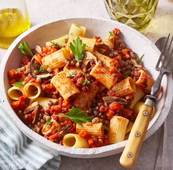 Rigatoni Nudeln mit veganer Linsenbolognese mit Champignons angerichtet auf einem Pastateller