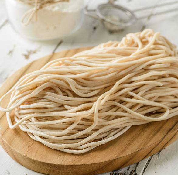 Veganer Nudelteig ohne Ei zu langen Nudeln geformt auf einem Holzbrett