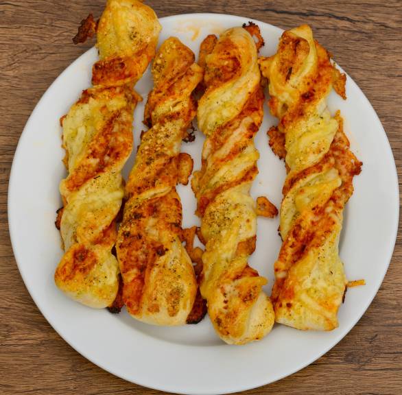 Vier selbst gebackene, gedrehte Pizzastangen angerichtet auf einem Teller