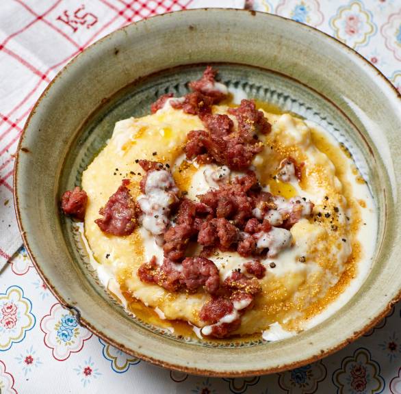 Polenta getoppt mit gebratener Salsiccia und Käsesoße angerichtet auf einem tiefen Teller