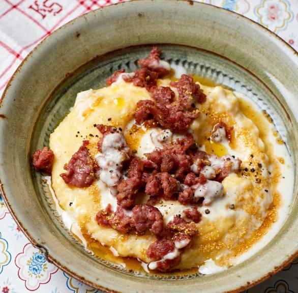 Polenta getoppt mit gebratener Salsiccia und Käsesoße angerichtet auf einem tiefen Teller