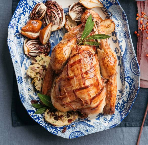 GanzePoulard mit Salsiccia-Reis-Füllung gebettet auf Radicchio-Birnen-Gemüse auf einer Servierplatte, daneben eine Sauciere mit Soße