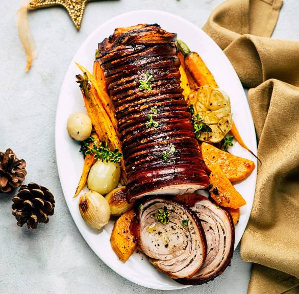 Schweinrollbraten angeschnitten auf einer Servierplatte, drumherum gebackene Süßkartoffeln und Karotten