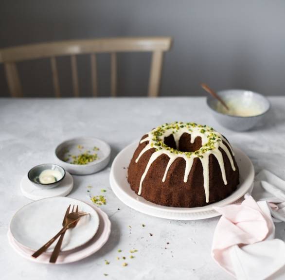 Pistazien-Marzipan-Gugelhupf mit weißem Schokoguss und Pistazienkernen auf einer Kaffeetafel