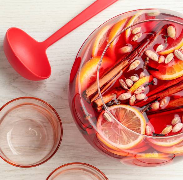 Silvesterbowle mit Früchten und Gewürzen in einer großen Glasschüssel, daneben eine Kelle und mehrere Gläser auf einem Tisch