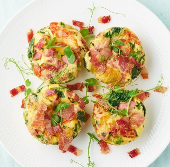 Vier Low-Carb-Frittata-Frühstücks-Muffins mit Ei, Spinat und Pancetta auf einem Teller