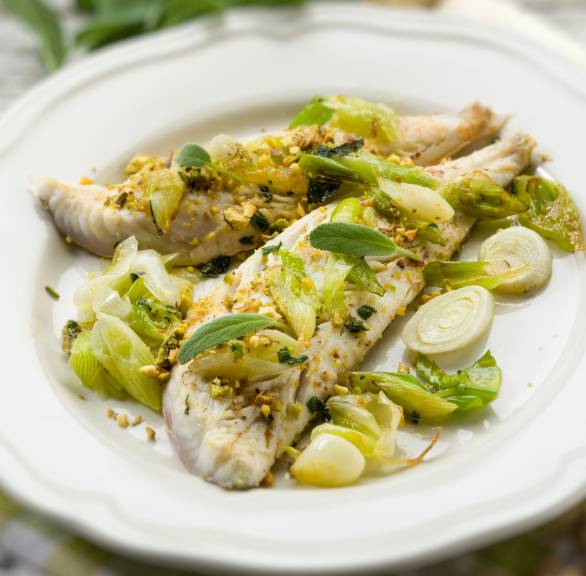 Zwei gebratene Kabeljaufielts auf einem Teller mit Porreeringen und gerösteten Pistazien