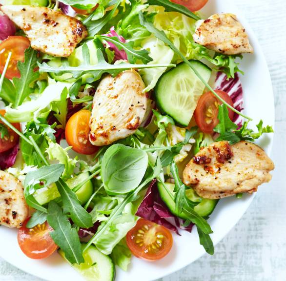 Gemischter bunter Salat getoppt von gebratenen, marinierten Putenbruststücken auf einem Teller