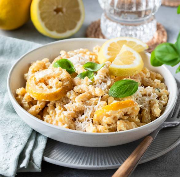 Topf mit One Pot Pasta mit frischer Zitronen-Ricotta-Soße sowie ein angerichteter Teller auf einem Tisch