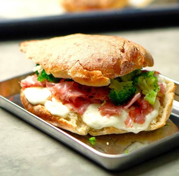 Selbstgebackenes, mit Käse, Schinken und Gemüse belegtes Sandwich aus Pizzateig Panuozzo napoletano auf einem Holzbrett